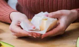 Dłonie rozwijają kostkę masła z papieru.